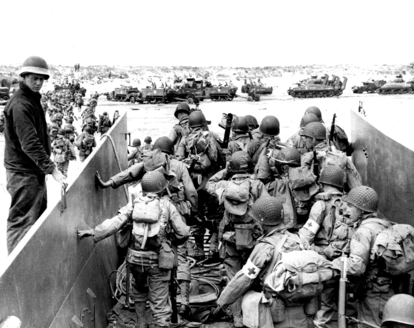 US Army soldiers disembark from a landing craft during the Normandy landings (D-Day) of June 6, 1944. Sherman tanks and White half-tracks can be seen drawn up on the beach. Pic courtesy of PA.