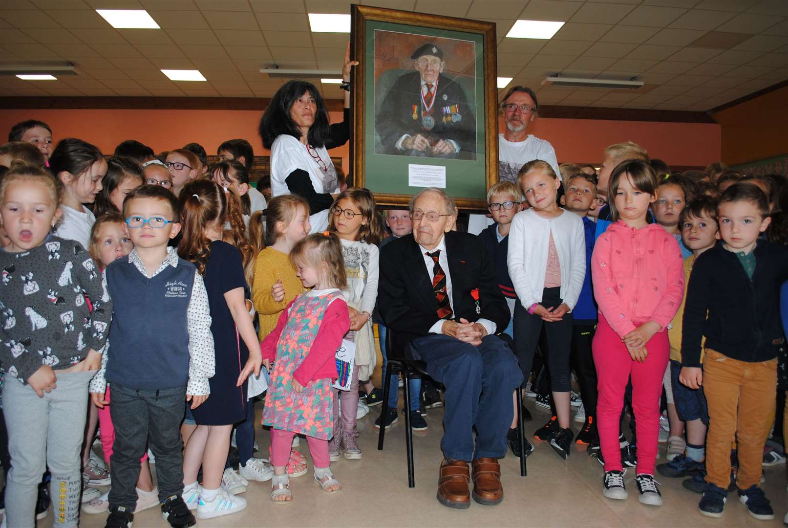 Cecil Newton visiting pupils at the Cecil Newton Primary School in June 2022. Behind him, teachers hold his portrait commissioned by HRH King Charles III