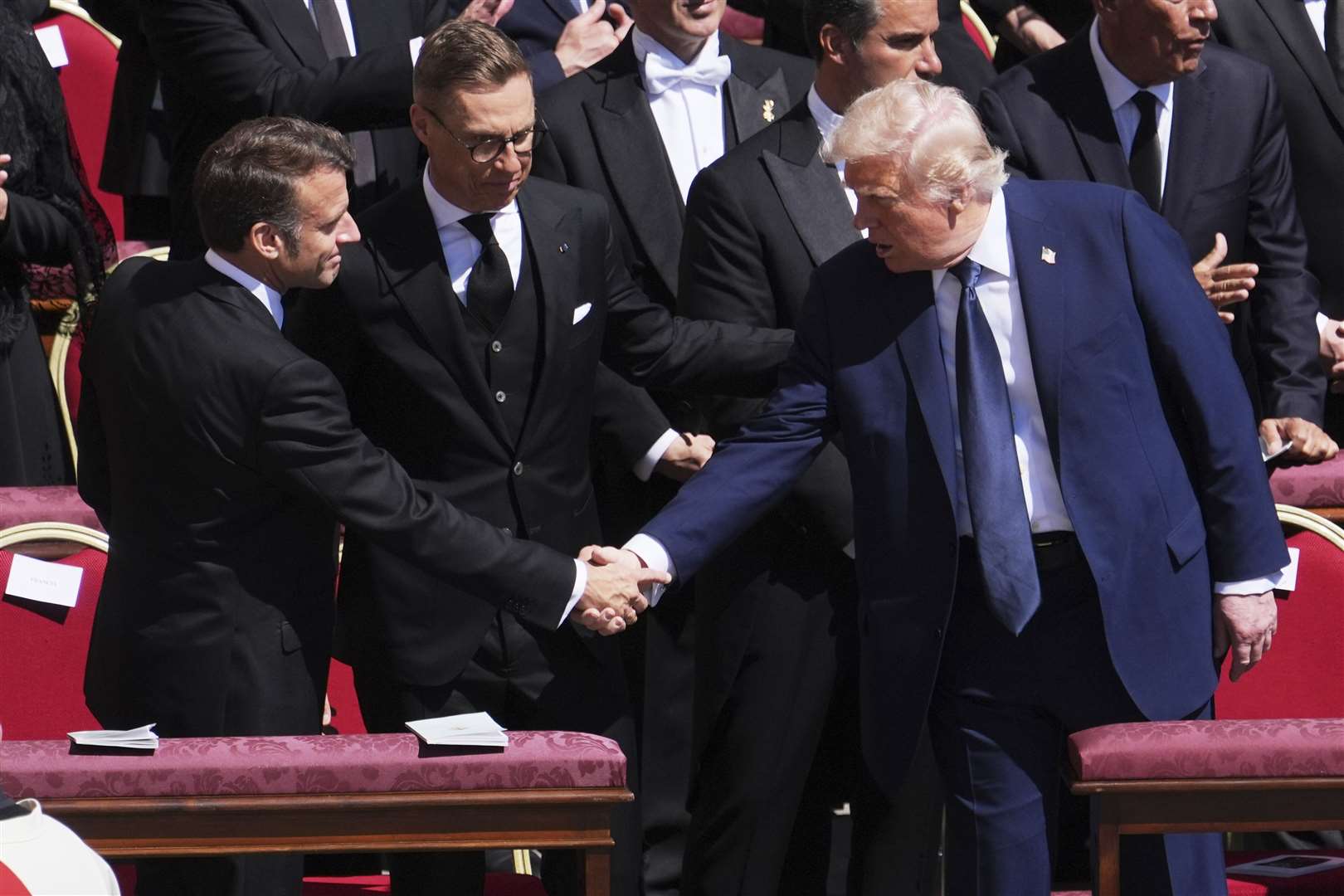 US President Donald Trump shakes hands with French President Emmanuel Macron as Finland’s President Alexander Stubb looks on, as they attend the funeral of Pope Francis (AP)