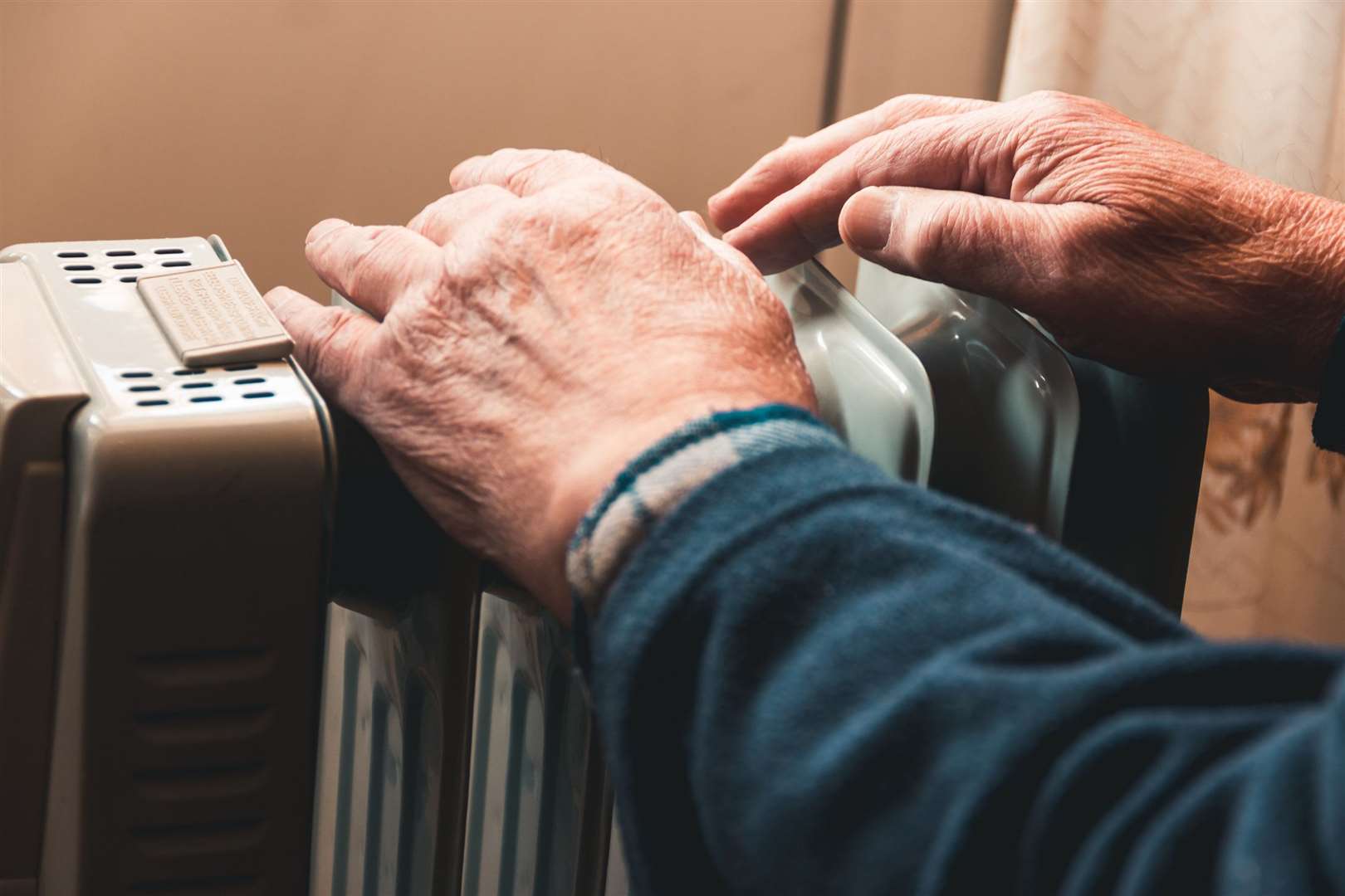 An elderly man warms his hands over an electric heater, energy bills (54657960)