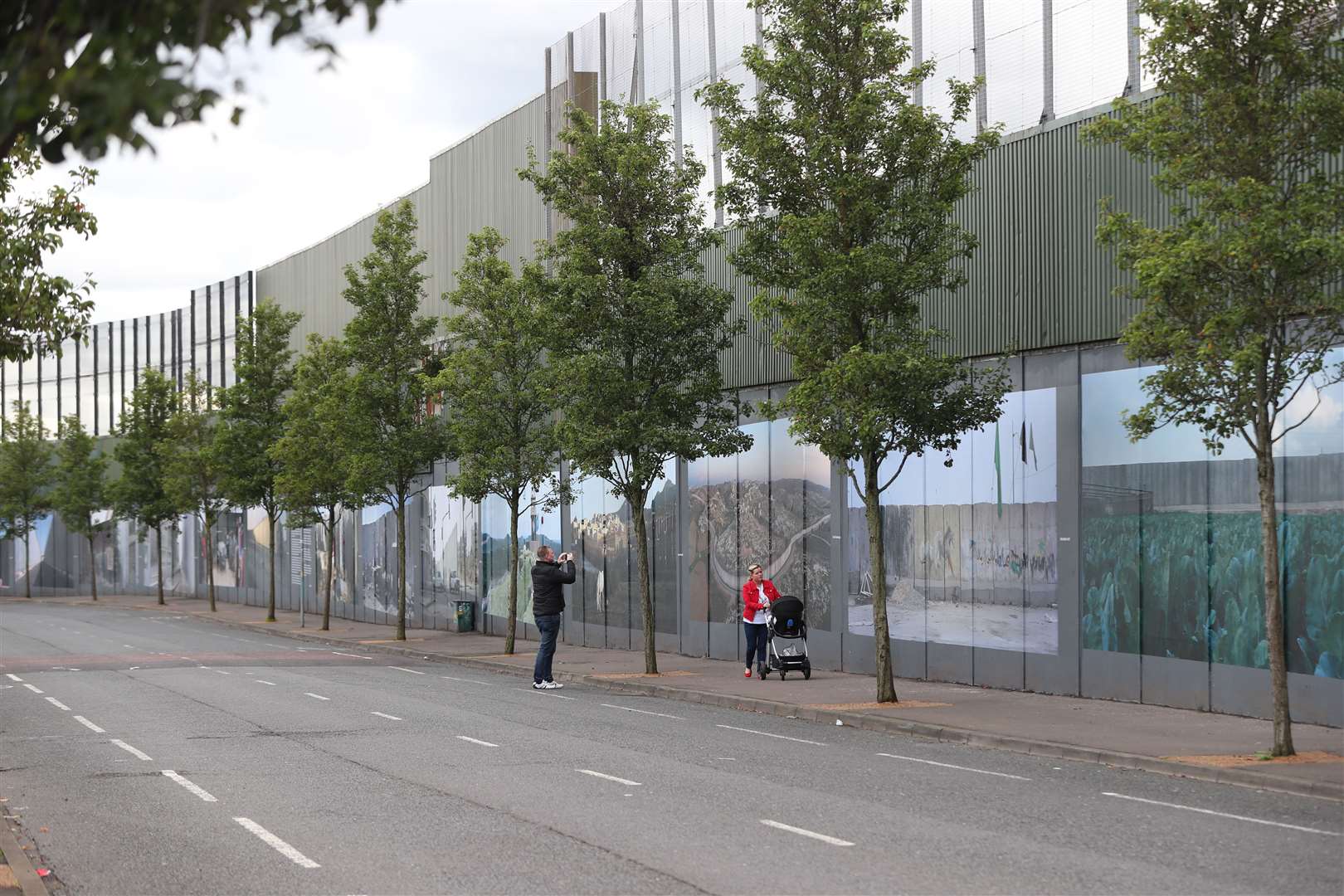 People walk past a peace wall in west Belfast that separates the unionist and nationalist communities in the area (Niall Carson/PA)