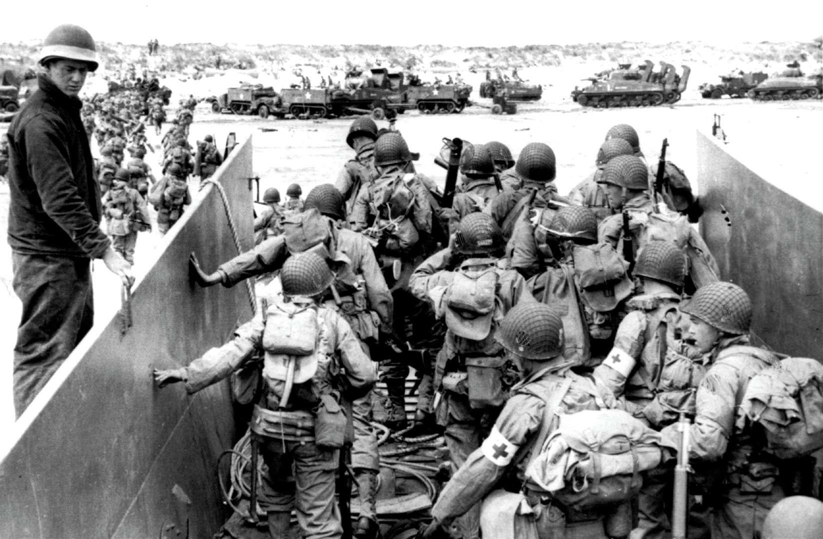 US Army soldiers disembark from a landing craft during the Normandy landings. Sherman tanks visible in the background. Credit: PA Photos/DPA, UK Use Only