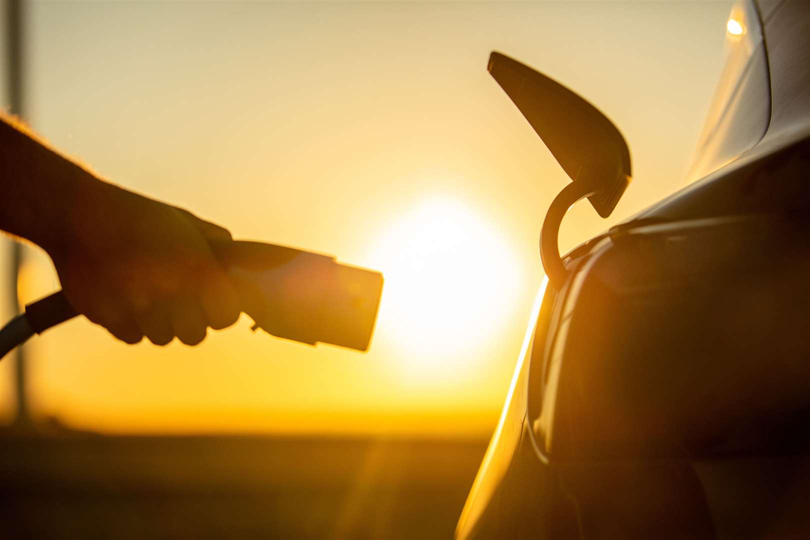 Close up of hand plugging electric charger to socket in electric car at sunrise (52735831)