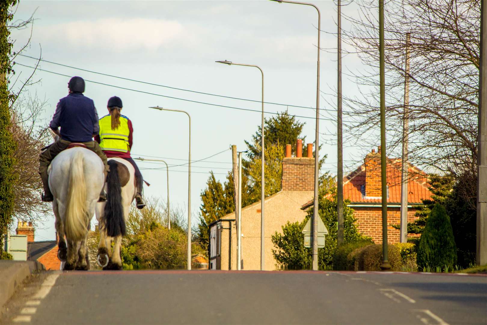 Two horse riders travel through a small village, on the main road. (59457600)