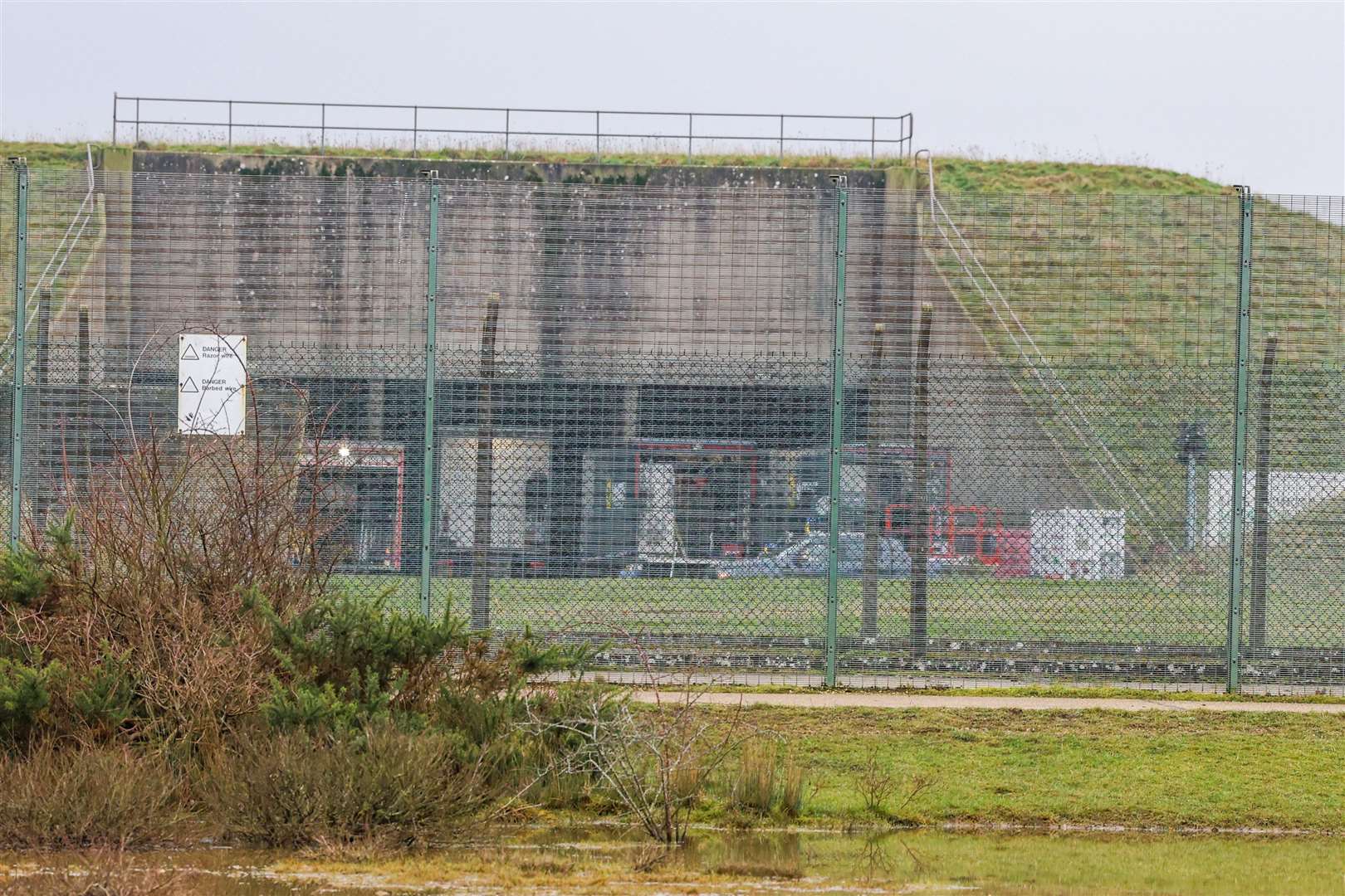 Production trucks visible behind the perimeter fence