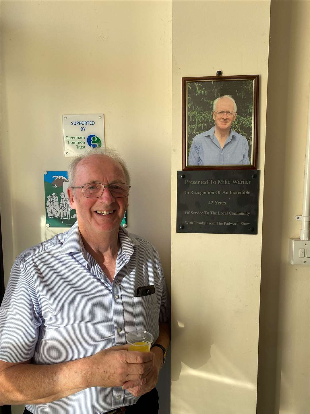 Mike Warner in front of a plaque put up in Padworth Village Hall to honour him